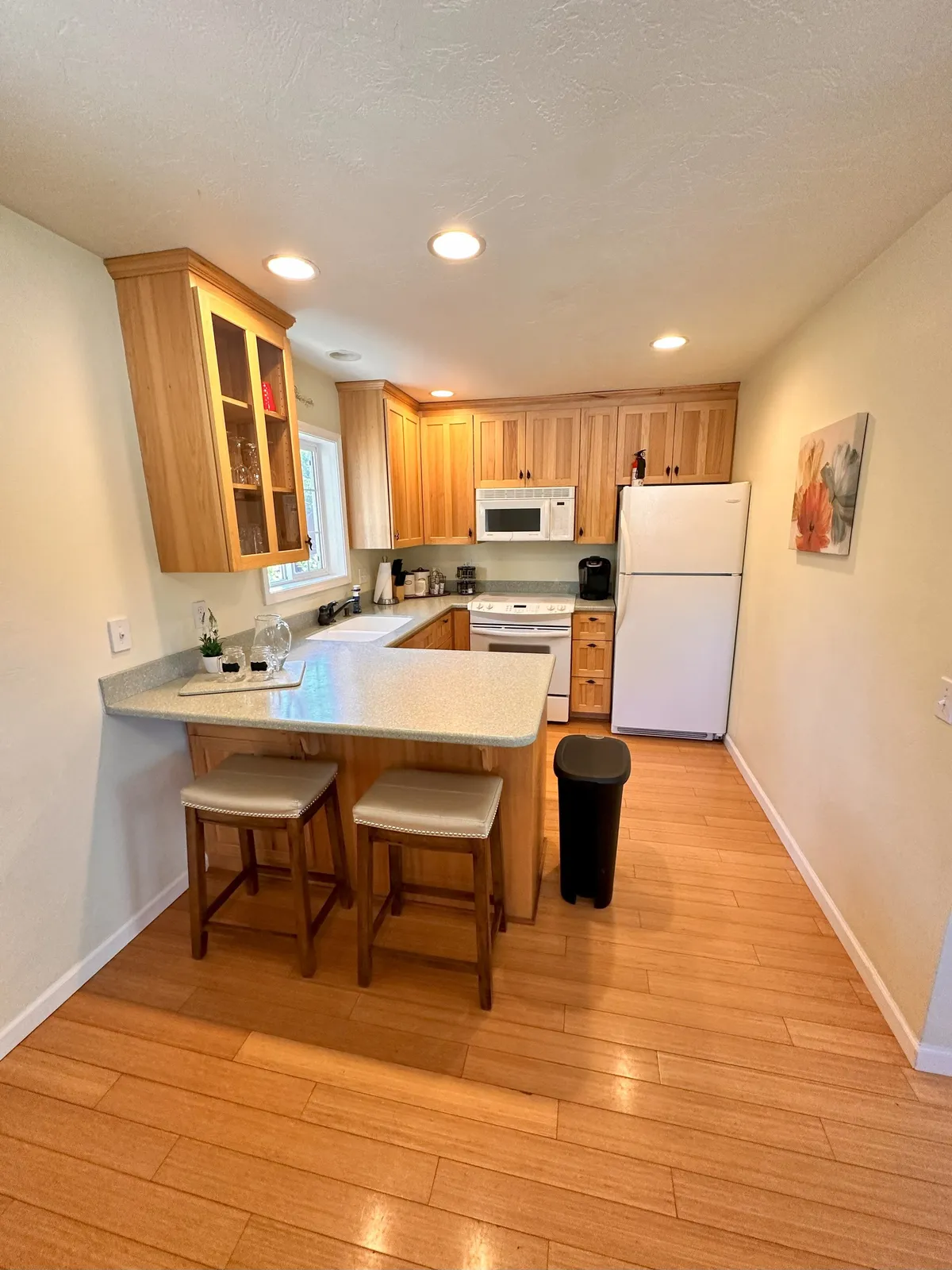 A warm, inviting kitchen with a gleaming granite countertop, wooden cabinets, stylish stools at the breakfast bar, and high-quality appliances. The space is flooded with natural light, suggesting a perfect place for morning coffee or socializing while preparing a meal.