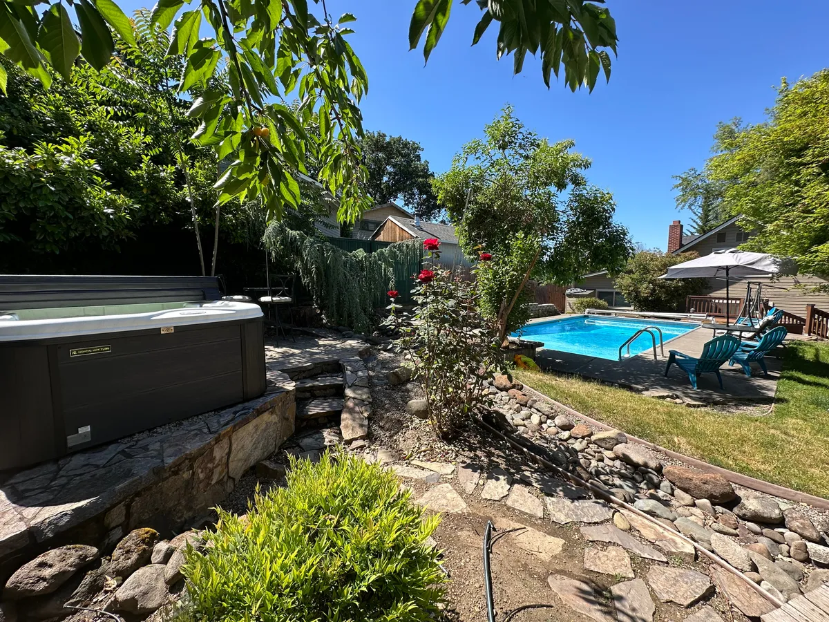 A tranquil backyard scene featuring a sparkling swimming pool and adjacent hot tub, surrounded by lush rose bushes and inviting lounge chairs. The area exudes a sense of relaxation and luxury, perfect for unwinding after a day of exploration.