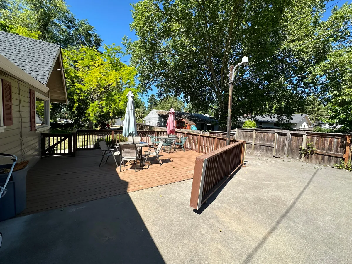 This image features a sunny outdoor deck with ample seating, umbrellas, and natural tree cover. The space is set up for outdoor dining, barbecues, and informal gatherings, illustrating a flexible environment suitable for both structured sessions and casual team interactions.