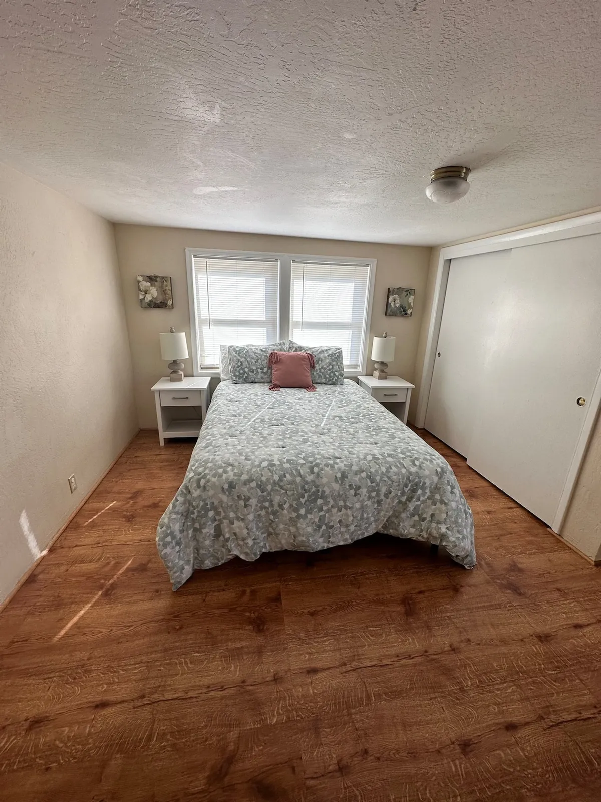 A tranquil bedroom featuring a bed with patterned bedding, two bedside lamps, and plenty of natural light streaming through the windows. The overall mood is peaceful and cozy, ideal for unwinding after a long day.