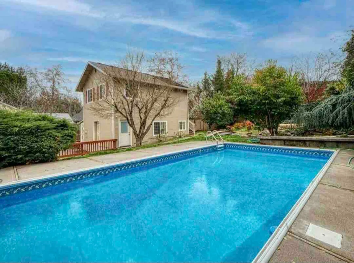 This image features a sparkling swimming pool in front of the house, surrounded by beautiful landscaping and spots for lounging or socializing. The relaxed mood suggests lazy afternoons, celebrations, or casual get-togethers.