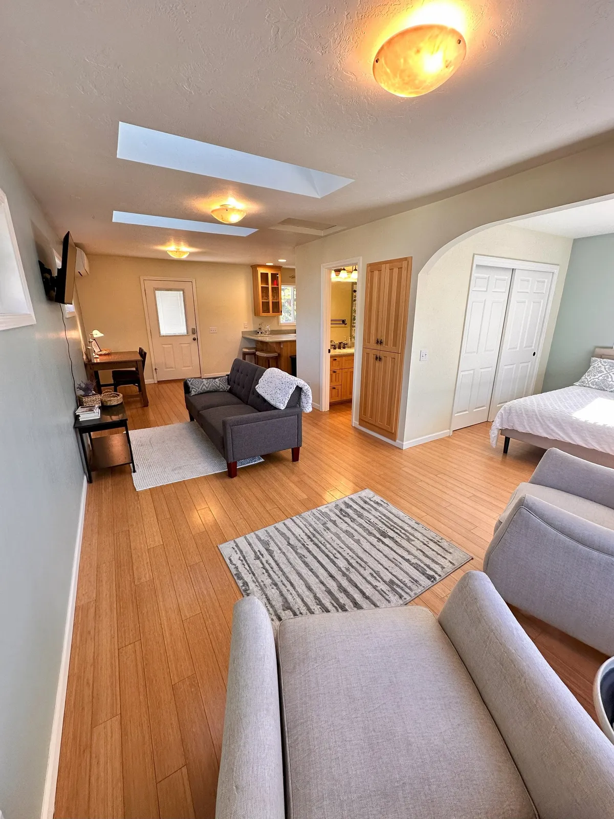 A sunlit open-plan living area featuring a cozy sofa, a stylish rug, and a spacious dining table. Large skylights and windows flood the room with natural light, creating an inviting space ideal for gatherings. The dining area sits adjacent to the living zone, emphasizing togetherness and connection.