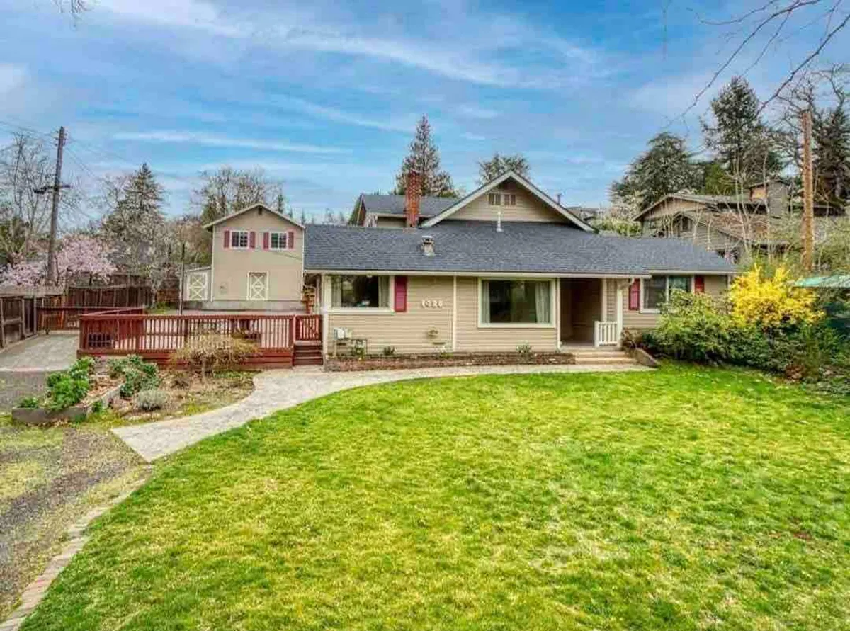 A welcoming exterior view of the property’s front porch, overlooking a manicured green lawn and surrounded by flowering trees. A spacious deck area hints at outdoor gatherings and relaxing evenings.