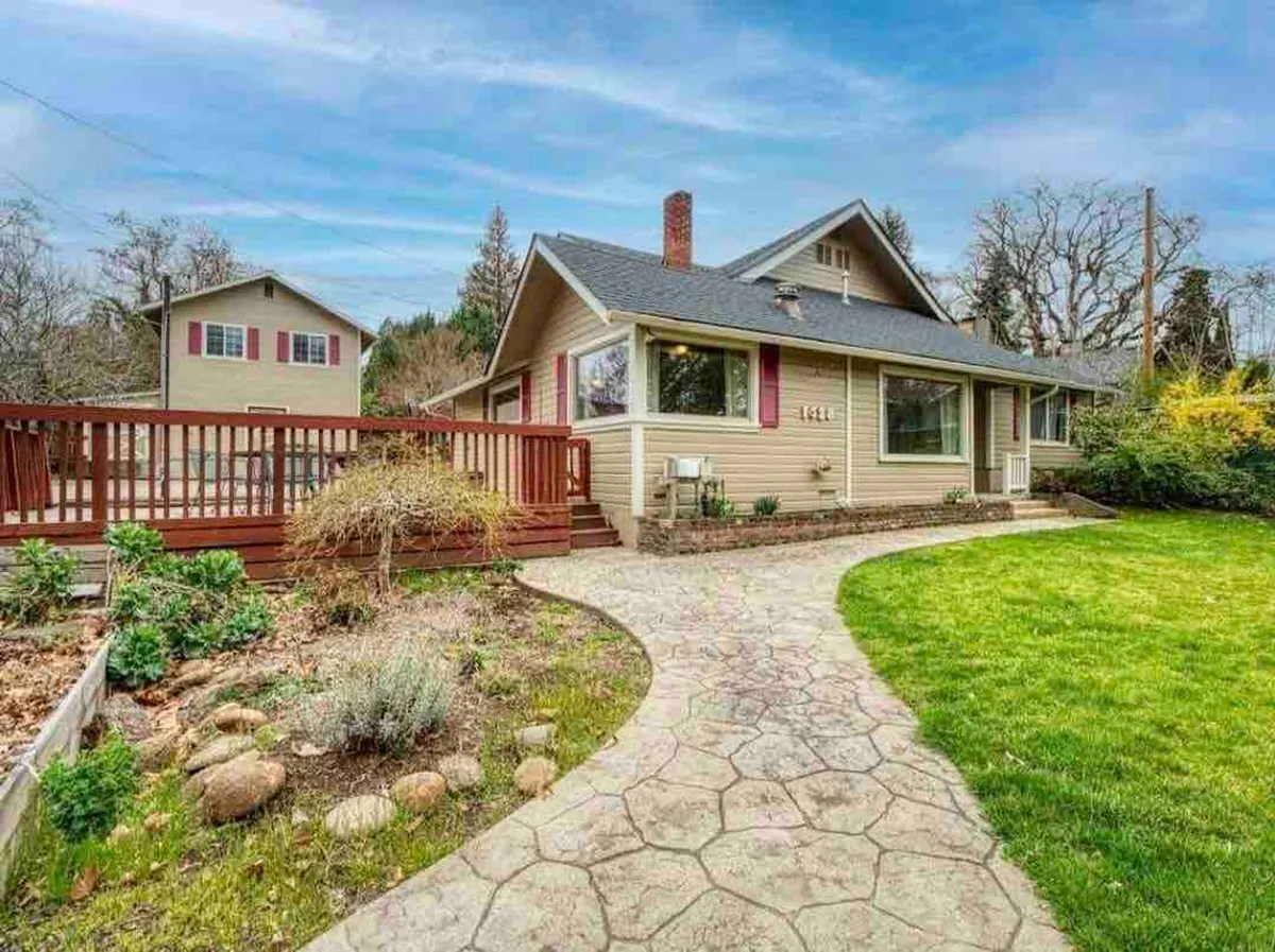 This image showcases the front porch of the main house, surrounded by a vibrant garden area and a welcoming stone pathway. The facade of the house is visible, exuding a warm, inviting atmosphere perfect for arrivals and group gatherings. Sunset light enhances the charm of the outdoor space, suggesting the potential for both daytime collaboration and evening relaxation.